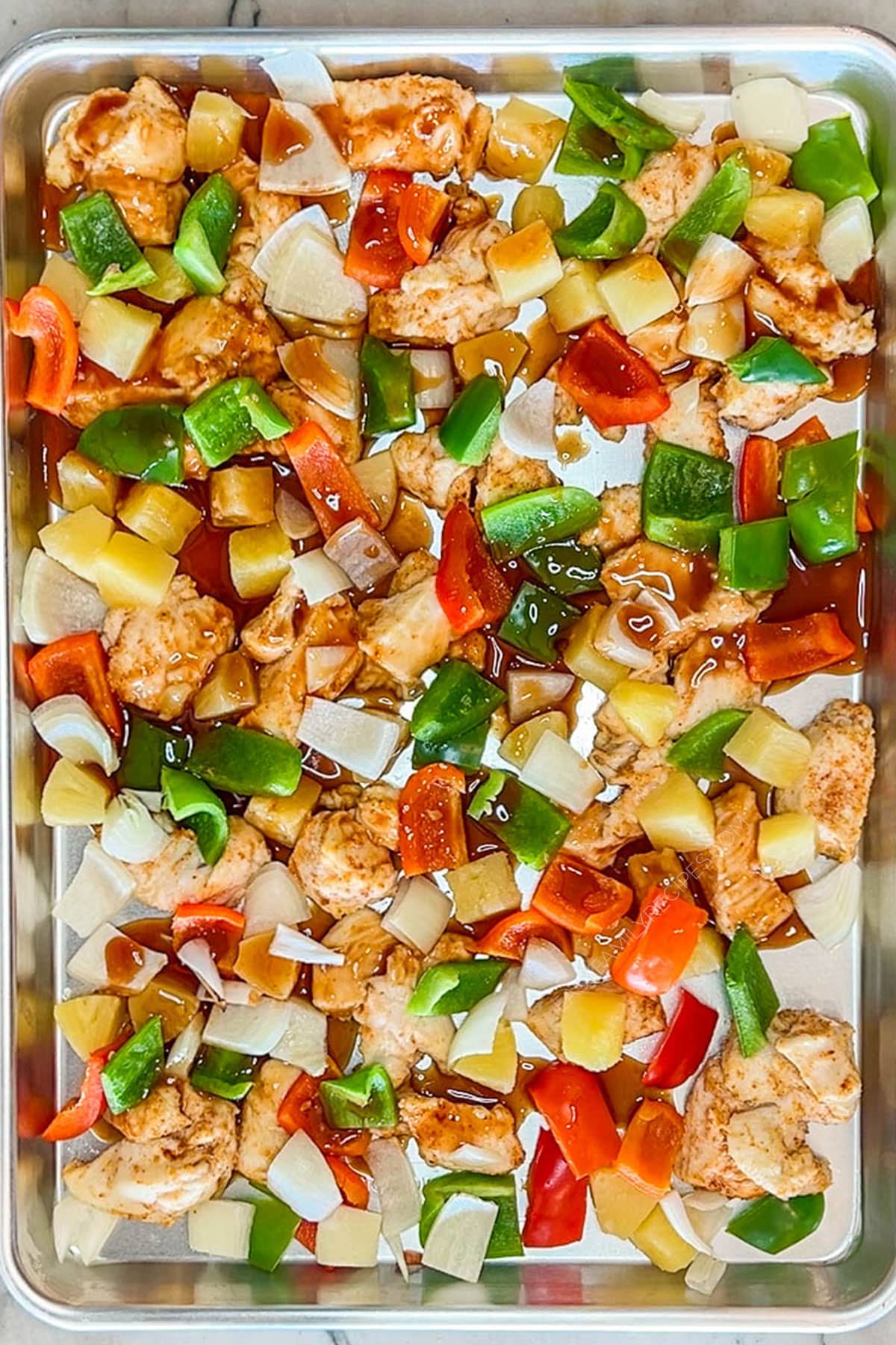 Sweet and sour sauce poured over the chicken and veggies on a sheet pan.