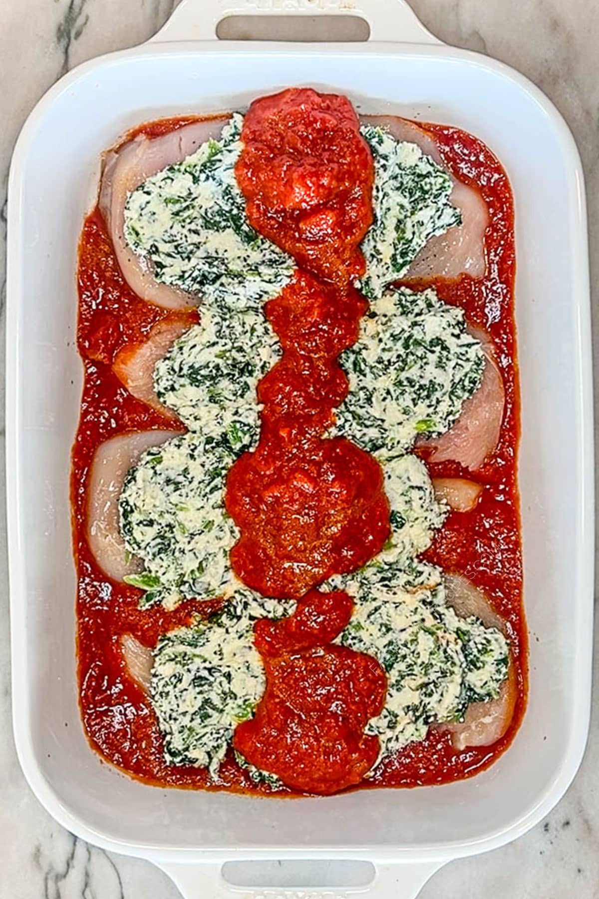 Ricotta spinach mixture and more tomato sauce placed on top of chicken breasts.