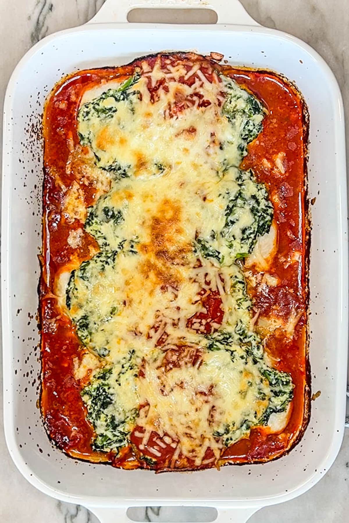 Baked spinach ricotta chicken in a white baking dish.