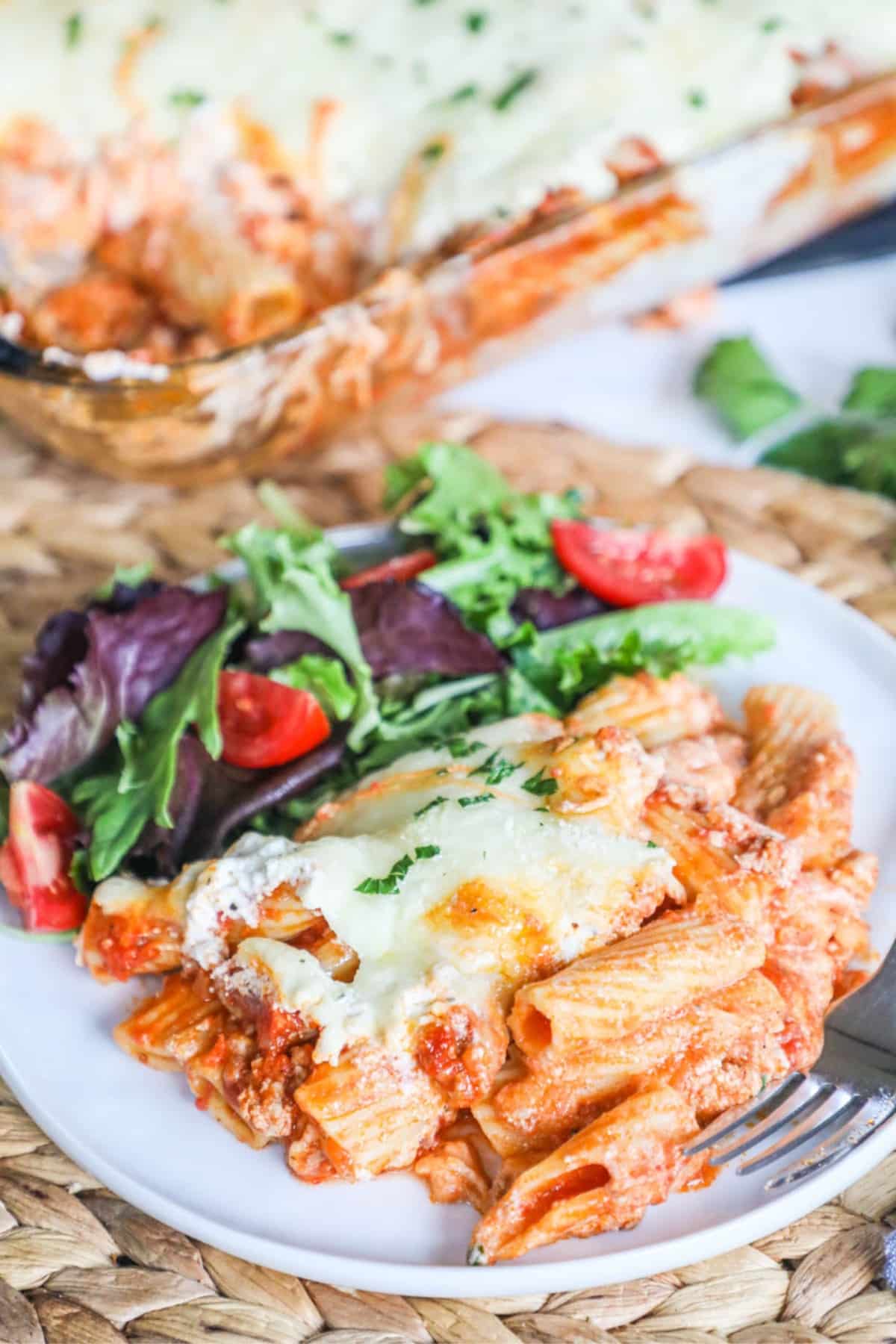 a serving of baked ziti on a white plate with a side of salad