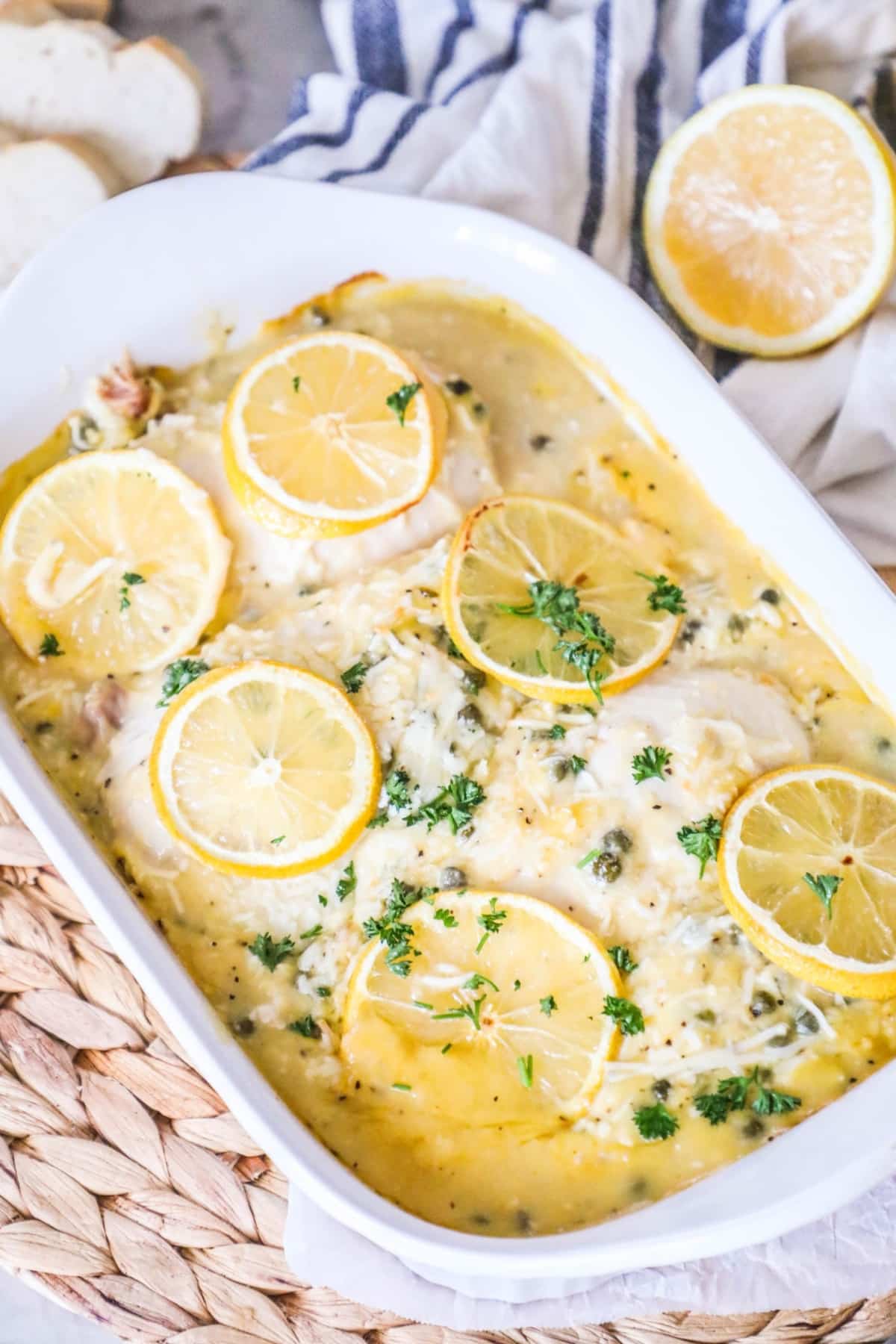 chicken piccata topped with lemon slices in a white casserole dish