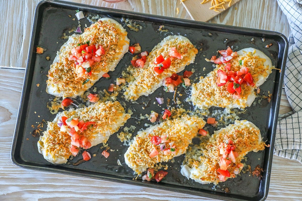 Overhead shot of six pieces of easy panko cheddar chicken on a sheet pan all topped with pico de gallo.