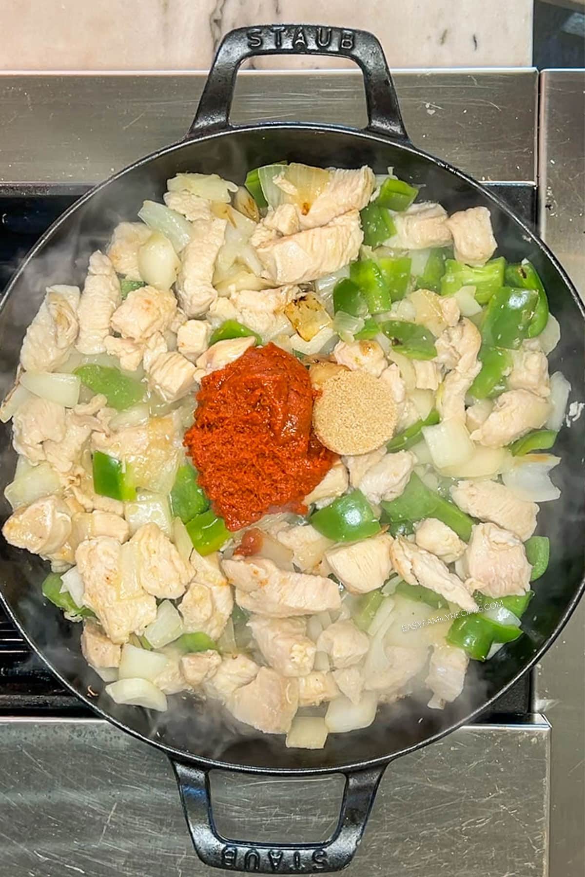 Curry paste and slices added to the chicken and veggies in a skillet.