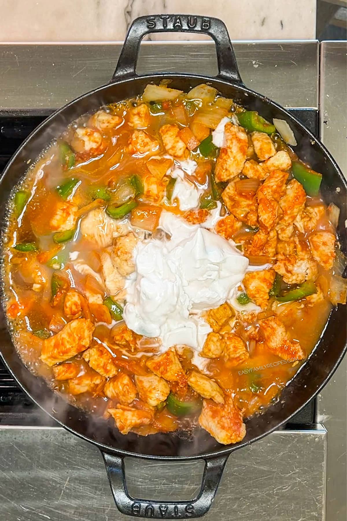Coconut cream added to the chicken curry in a skillet.