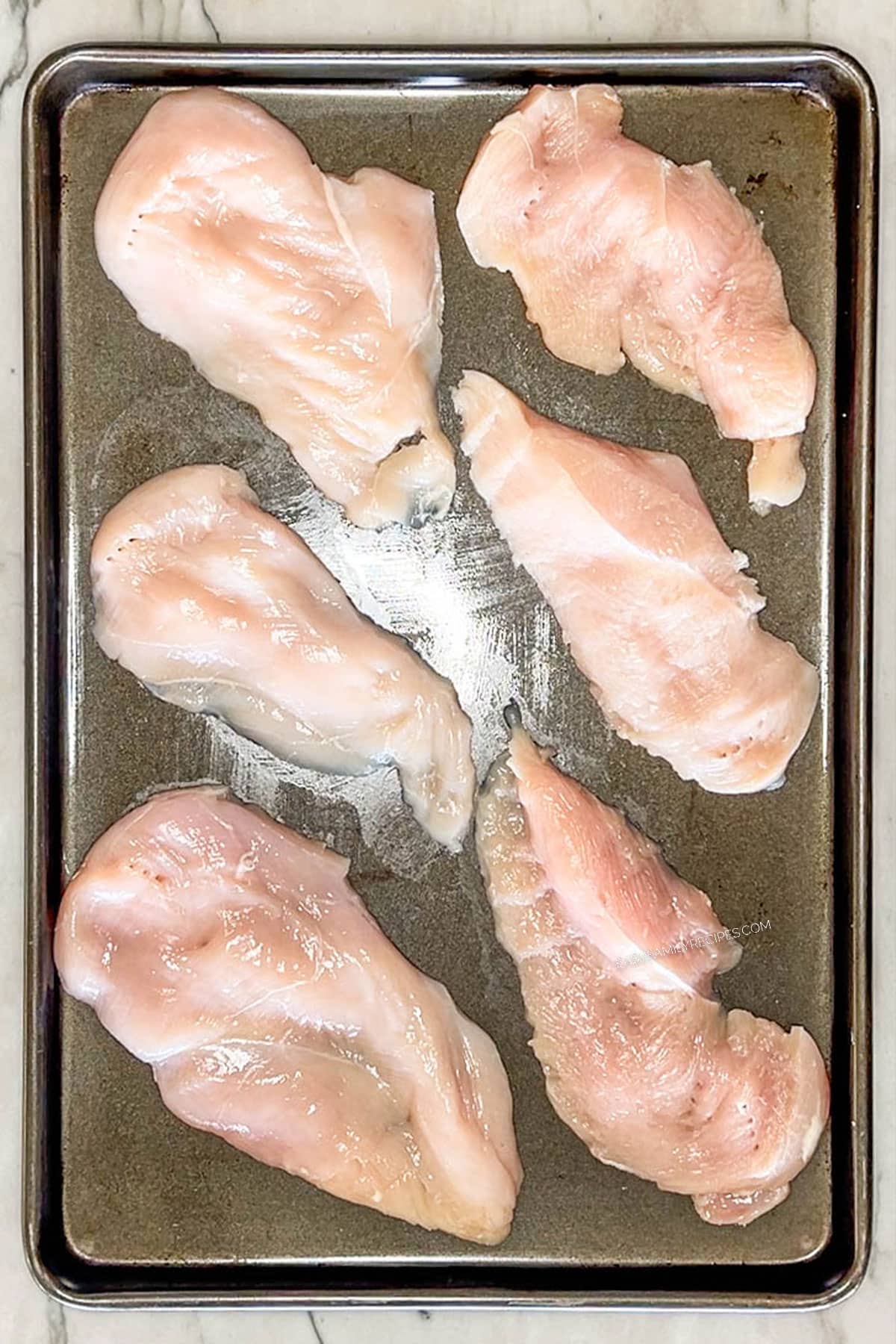 Six thinly sliced chicken breasts on a sheet pan.