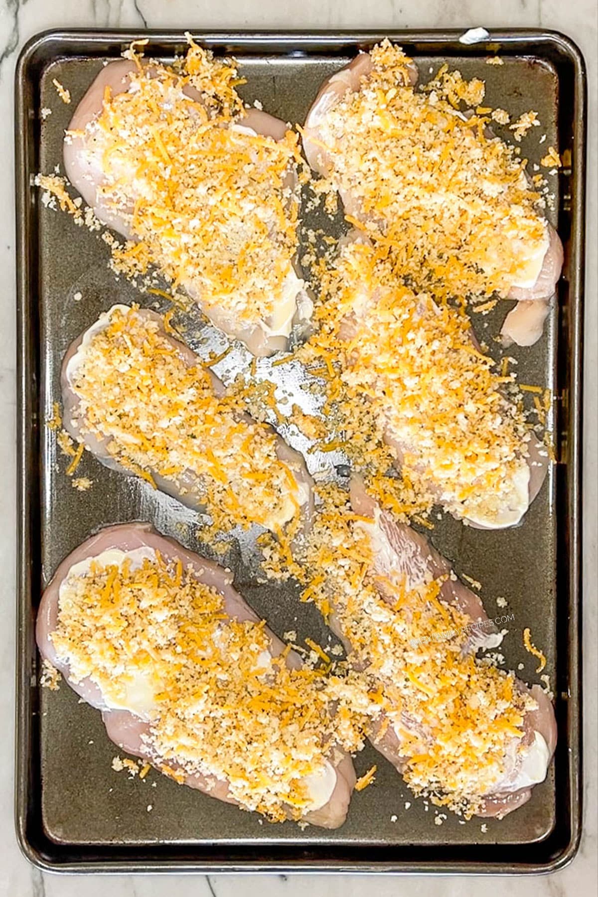 Chicken breasts on a sheet pan topped with mayo panko bread crumbs and cheddar on top.