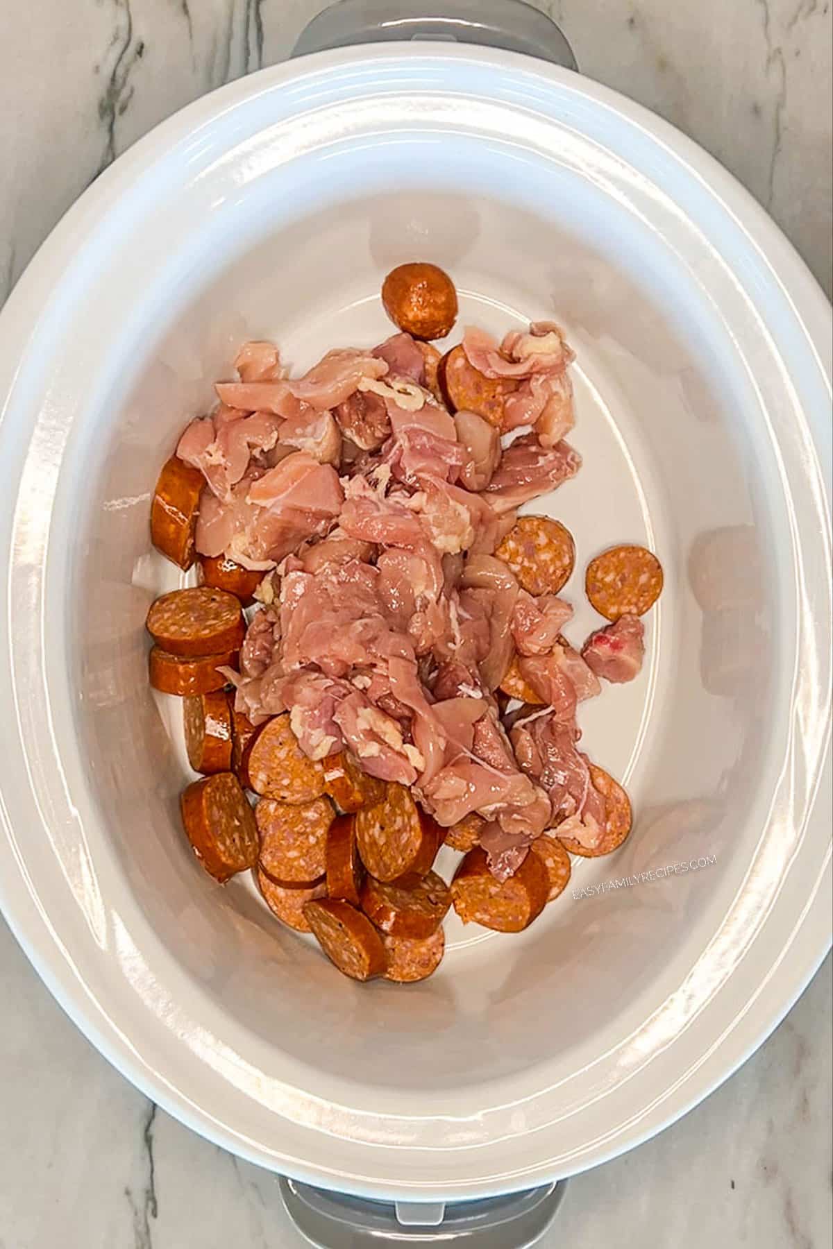 White crock pot with chicken and sausage.
