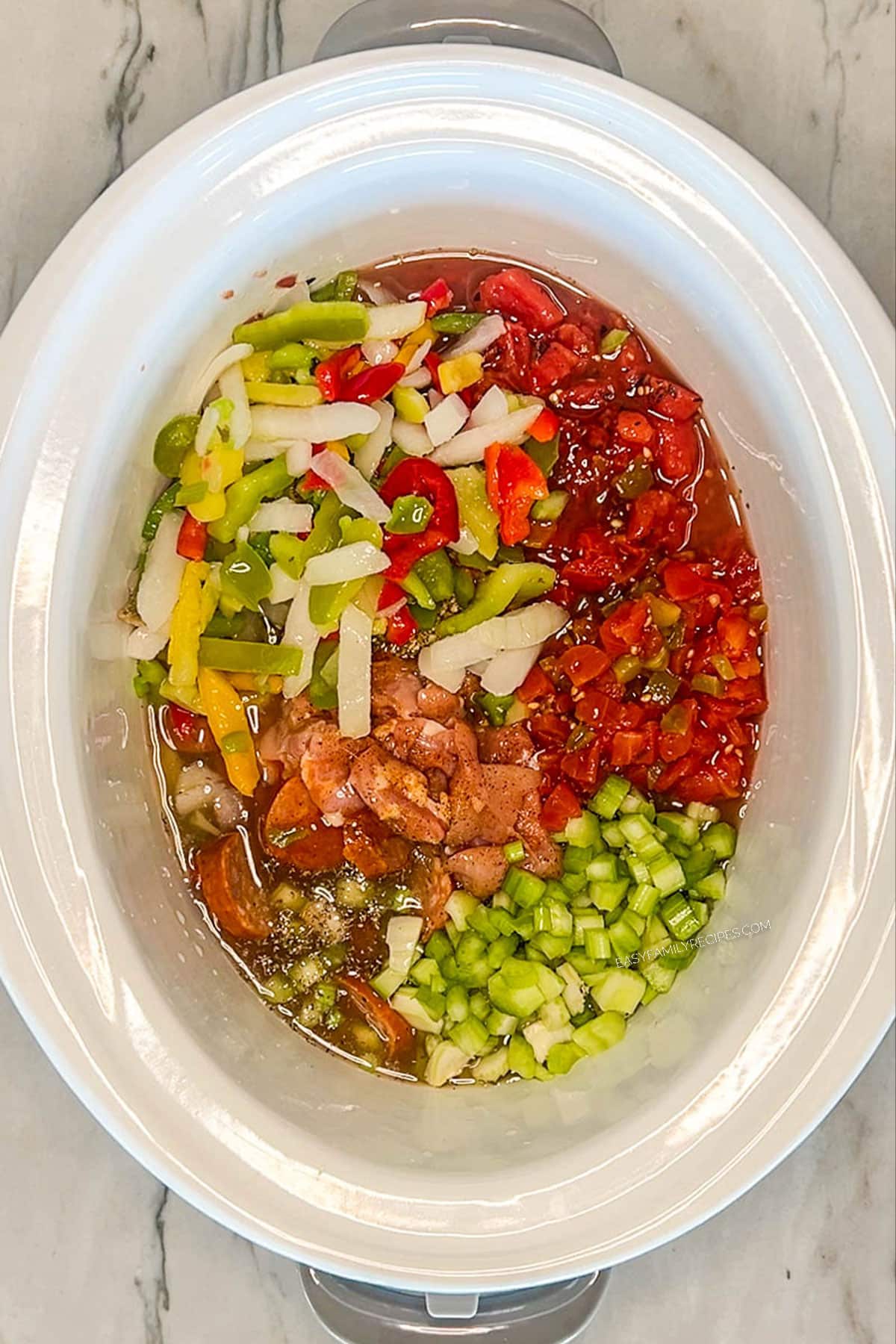 White crock pot with chicken, sausage, tomatoes, spices and vegetables.