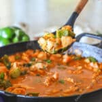 Serving spoon scooping up some chicken curry from a skillet.