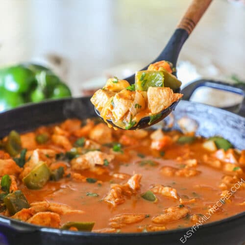 Serving spoon scooping up some chicken curry from a skillet.