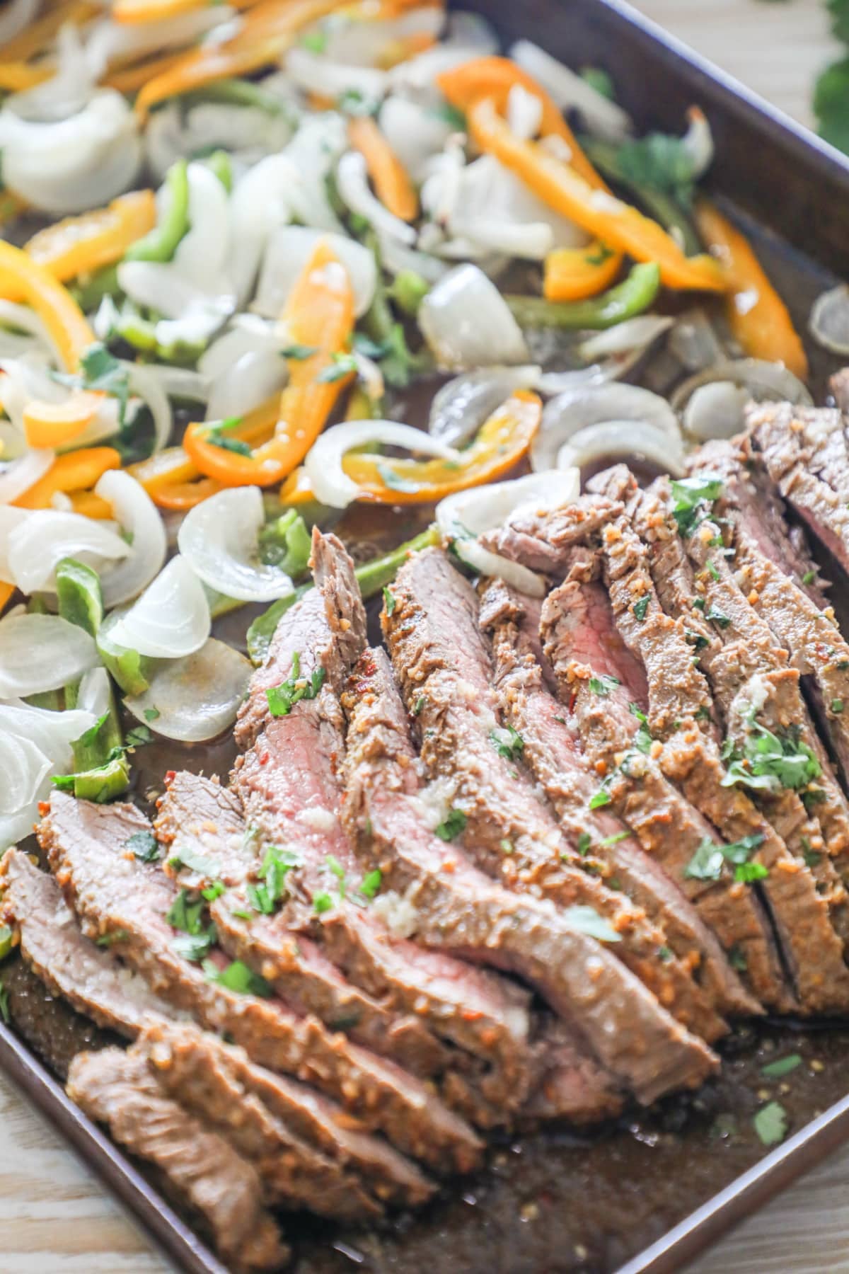 sliced flank steak with peppers and onions on a sheet pan for fajitas