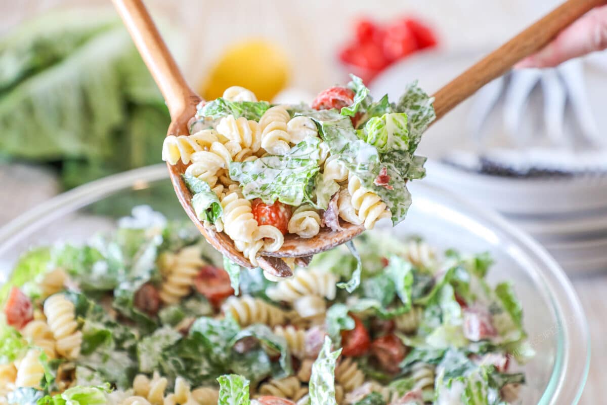 salad tongs being used to serve pasta salad out of a bowl.