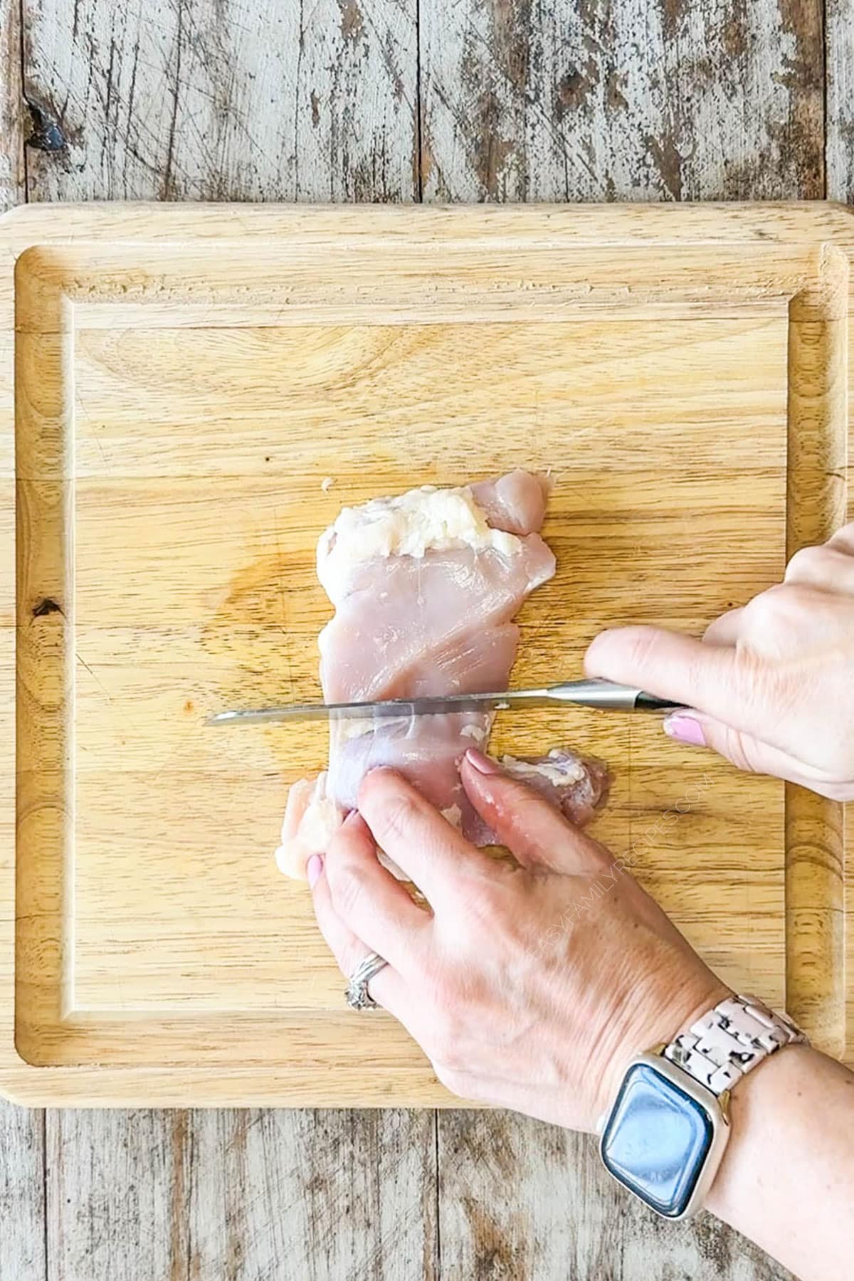 hand with knife cutting chicken thighs on wooden cutting board