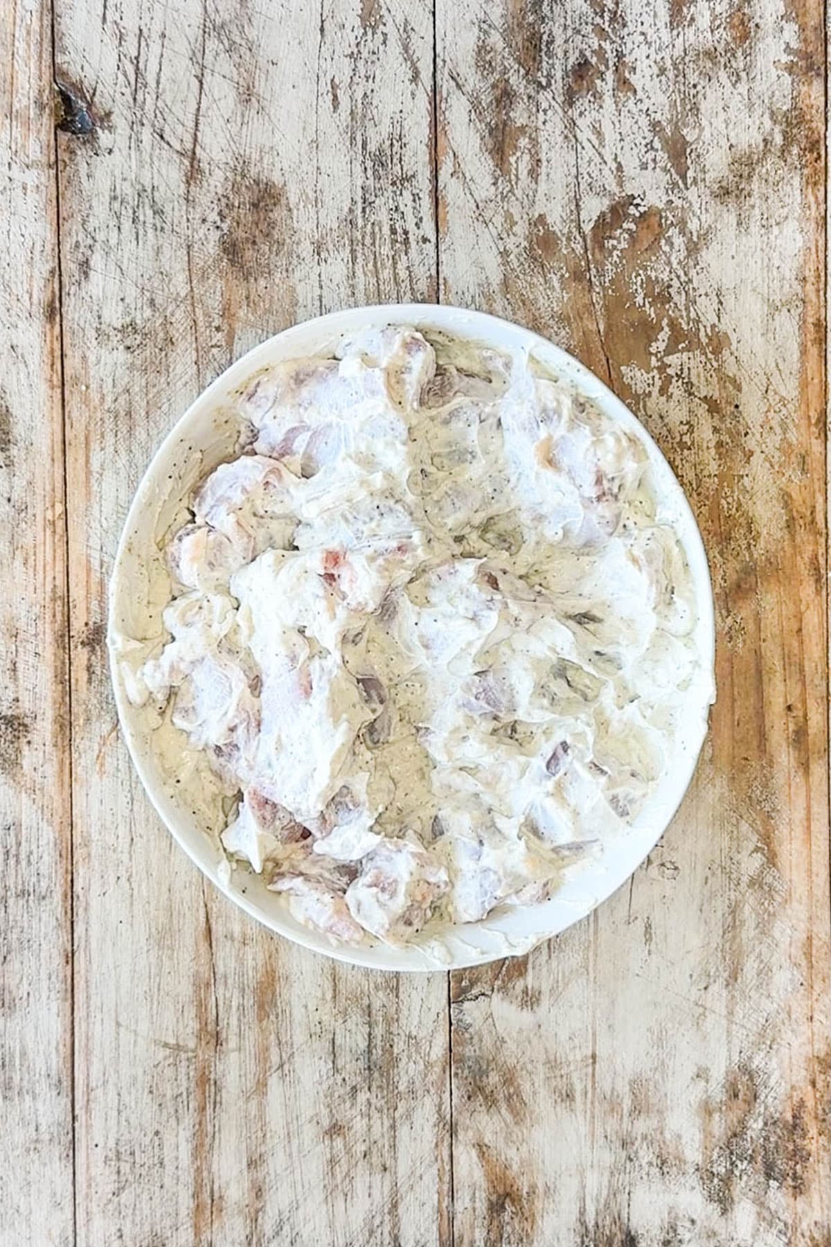 chicken bites coated in marinade- in white bowl on wooden background