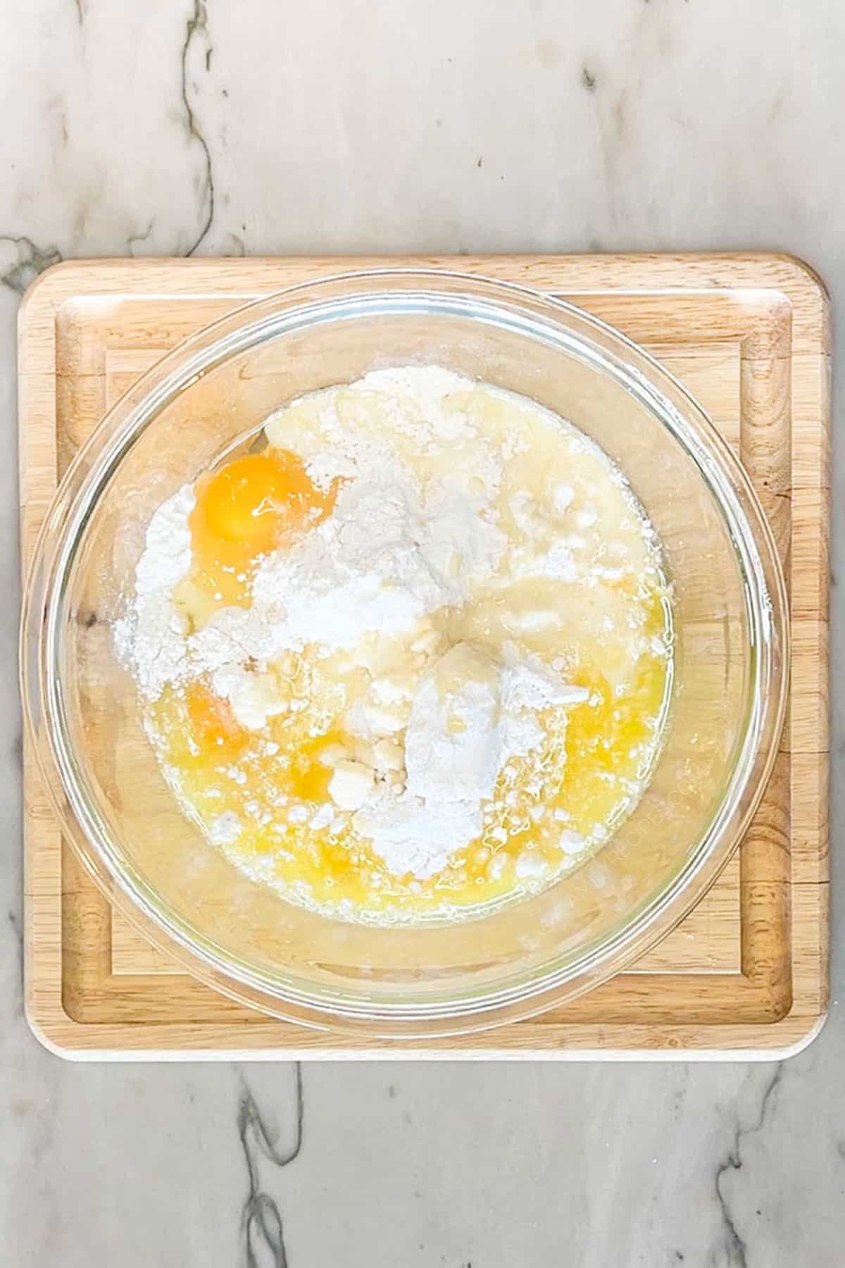 Ingredients for lemon cake mix crinkle cookies in a glass bowl. On a wooden board and background.