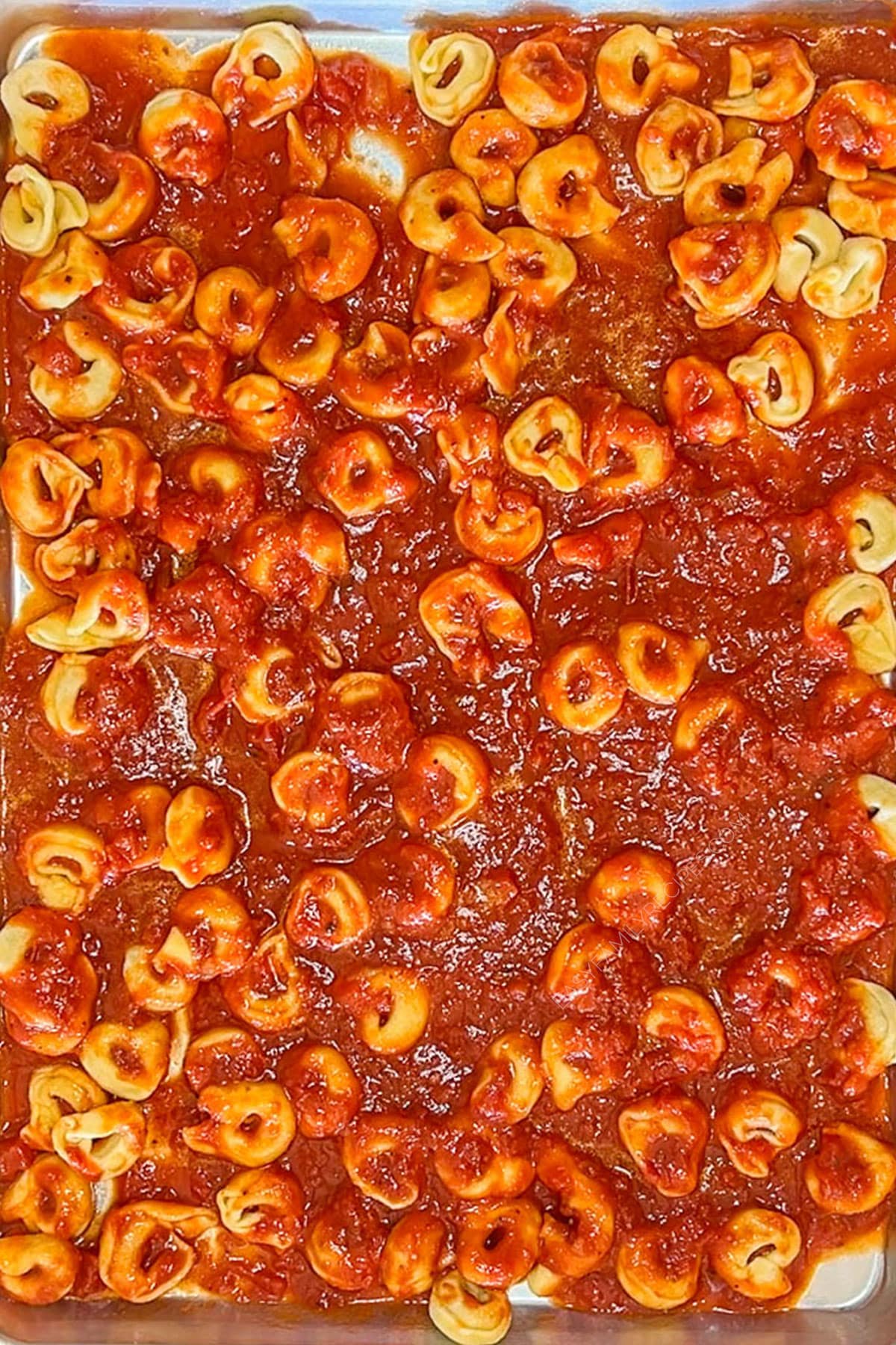 Tortellinis mixed with tomato sauce on a sheet pan.