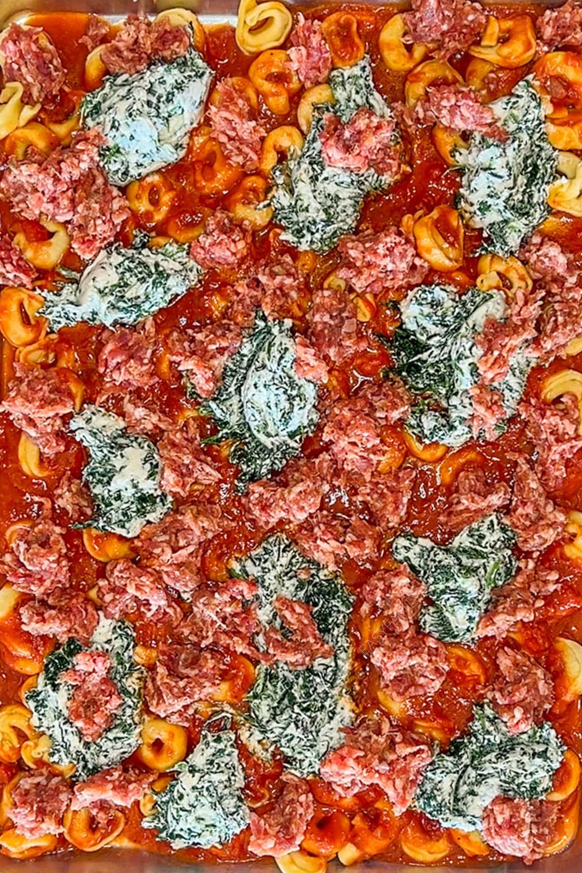 Spinach ricotta mixture dolloped on top of the pasta and sausage on a sheet pan.
