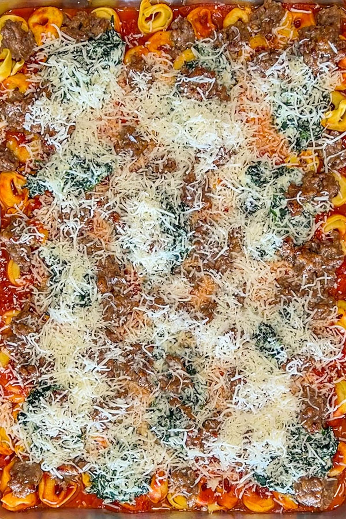 Cheeses added on top of the sausage and tortellini mixture on a sheet pan.