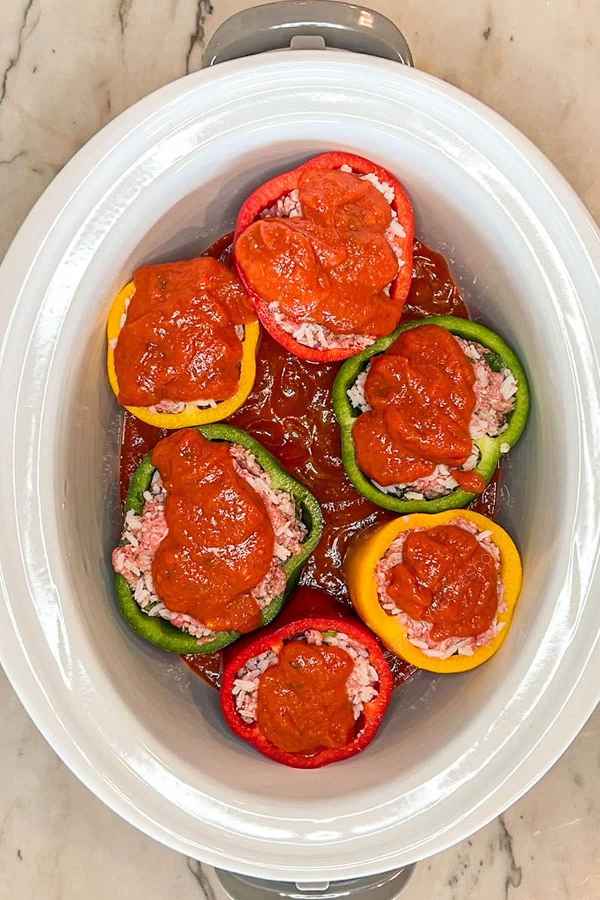 White crockpot with slow cooked stuffed peppers with marinara sauce