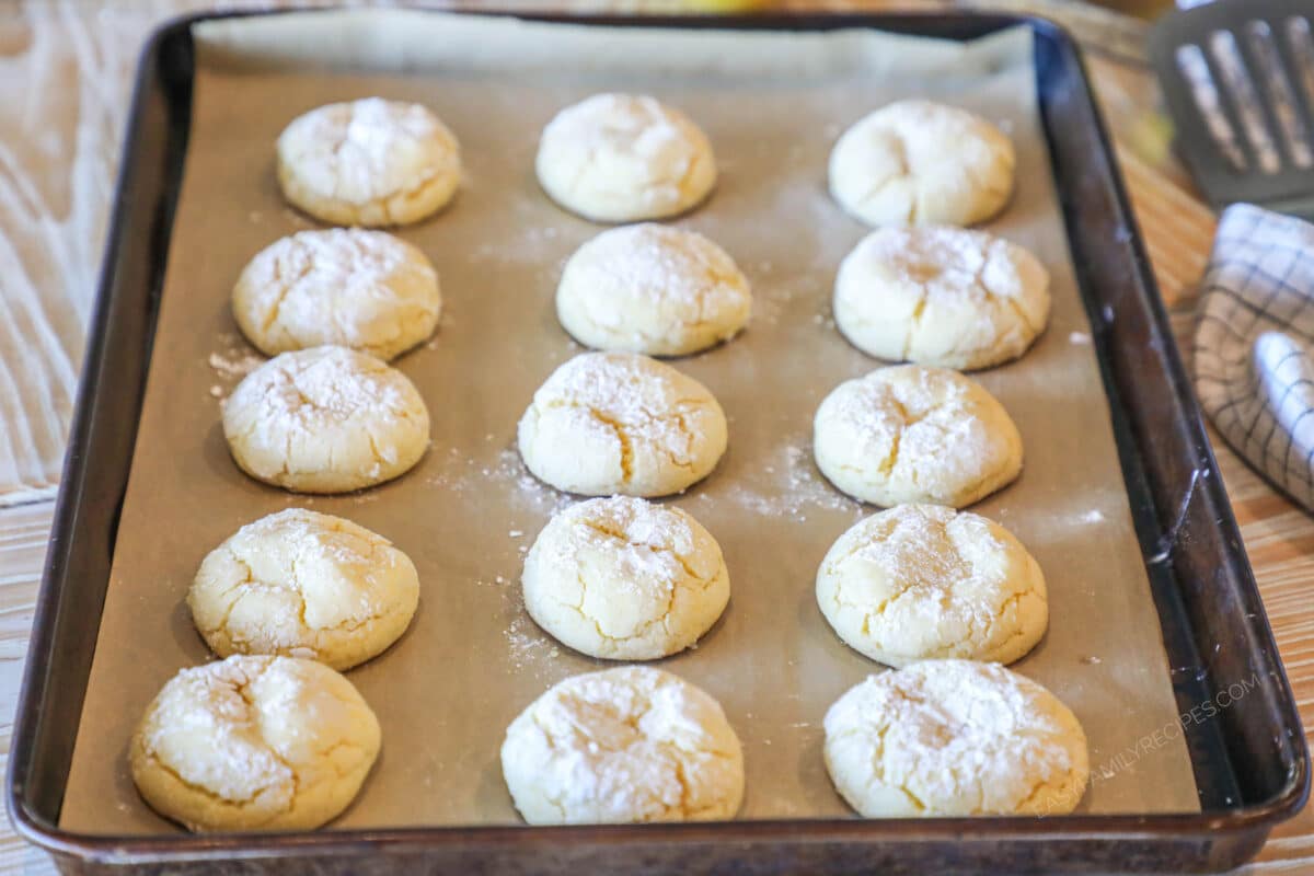 Lemon cake mix crinkle cookies on baking sheet with parchment paper. On a wooden background with a spatula and kitchen towel,