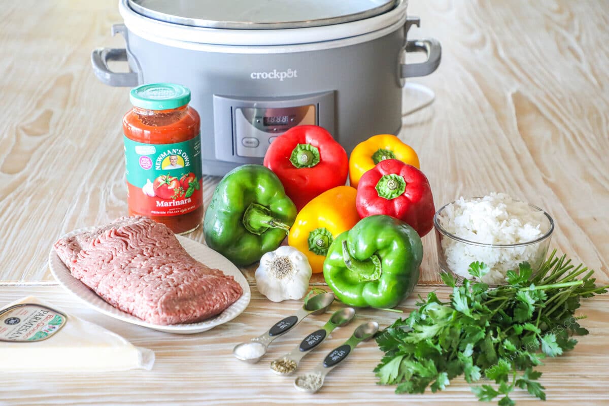 Ingredients for making slow cooker stuffed peppers in front of grey crockpot on a wooden background