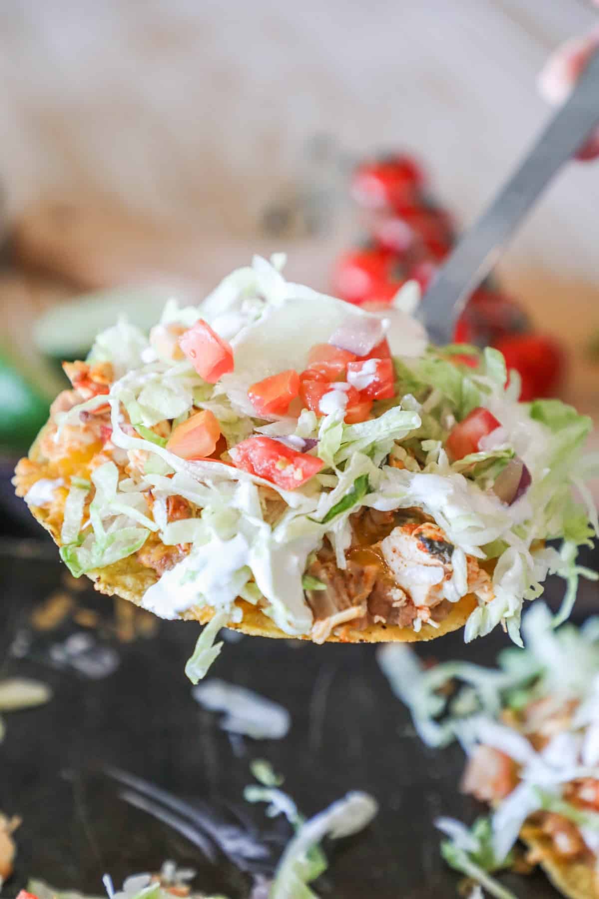 side view of a baked chicken tostada topped with lettuce, tomato, and sour cream.