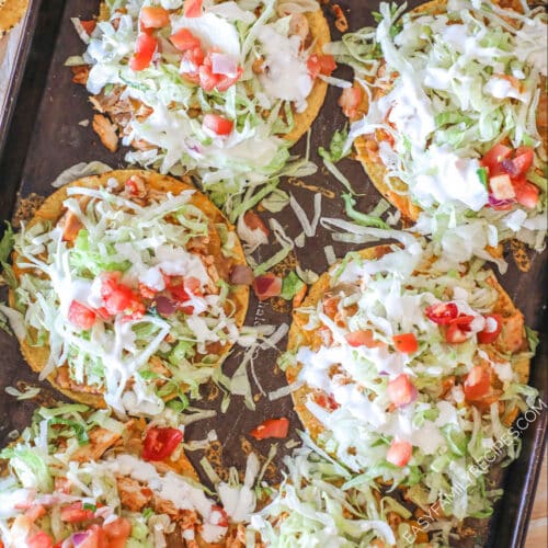 above image of baked tostadas piled with lettuce and tomato.