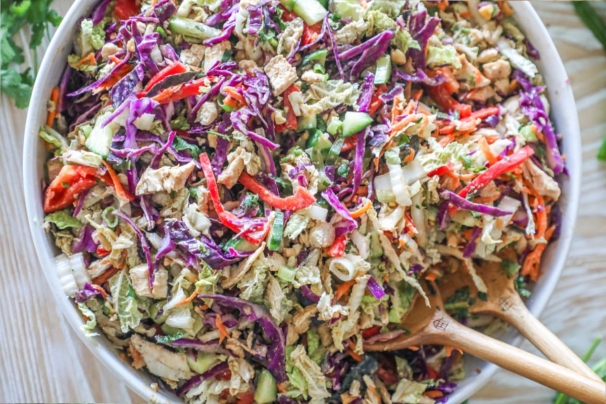 Thai Style Chicken Salad with Peanut Dressing in a large white bowl with wooden spoons
