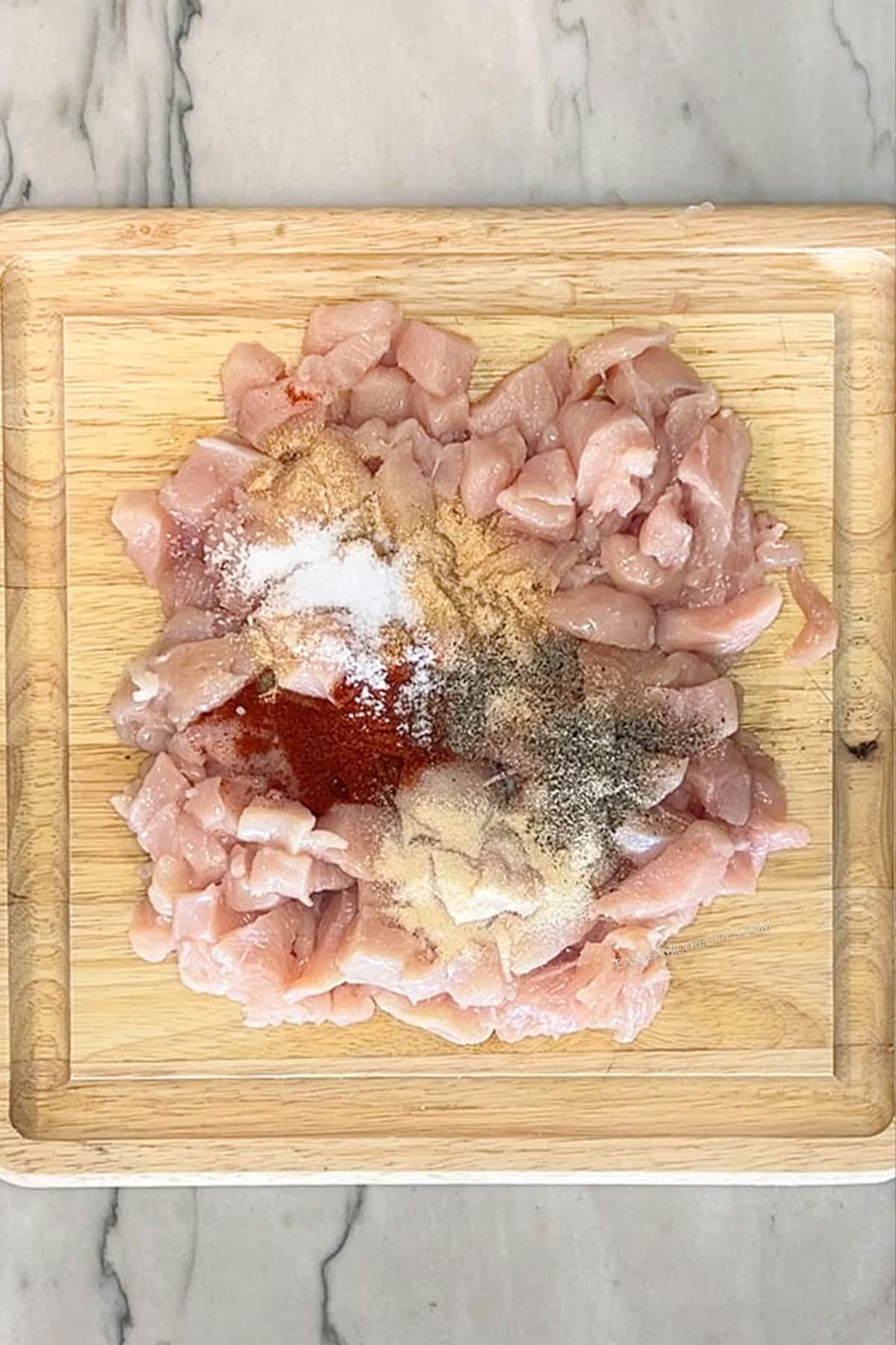 Cut chicken pieces with seasonings on top. On a wooden cutting board