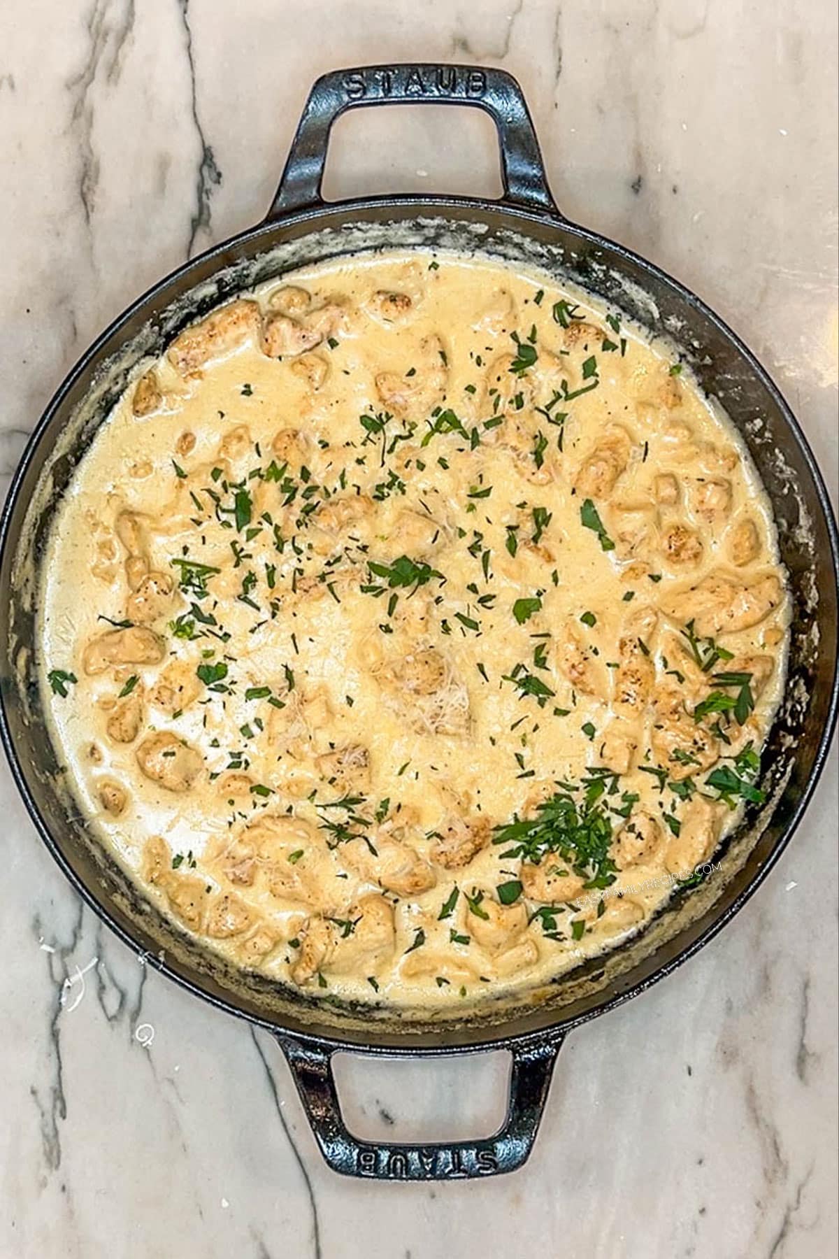 fresh herbs sprinkled on top of smothered chicken. In pan on a wooden background