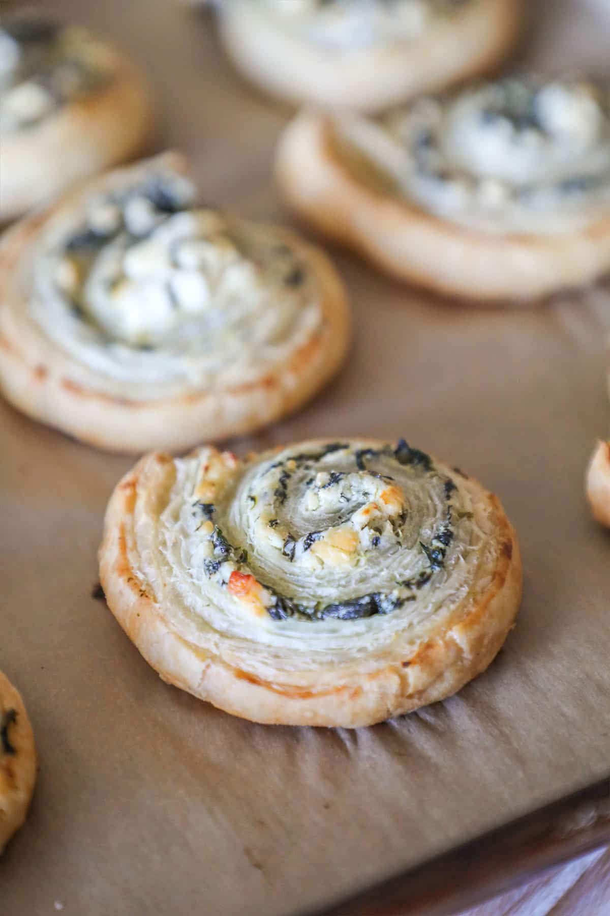 Close up of spinach feta puff pastry swirls on parchment paper lined baking sheet.