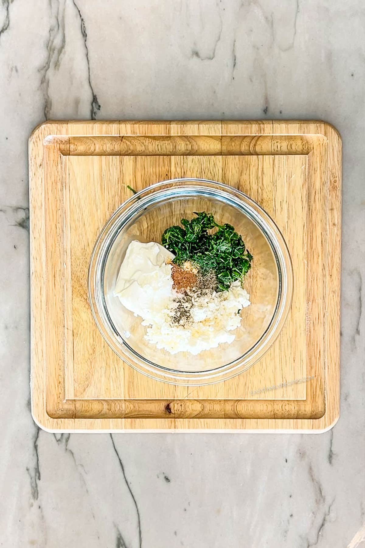 Spinach, feta, cream cheese & seasonings combined into a glass bowl. On a wooden board.