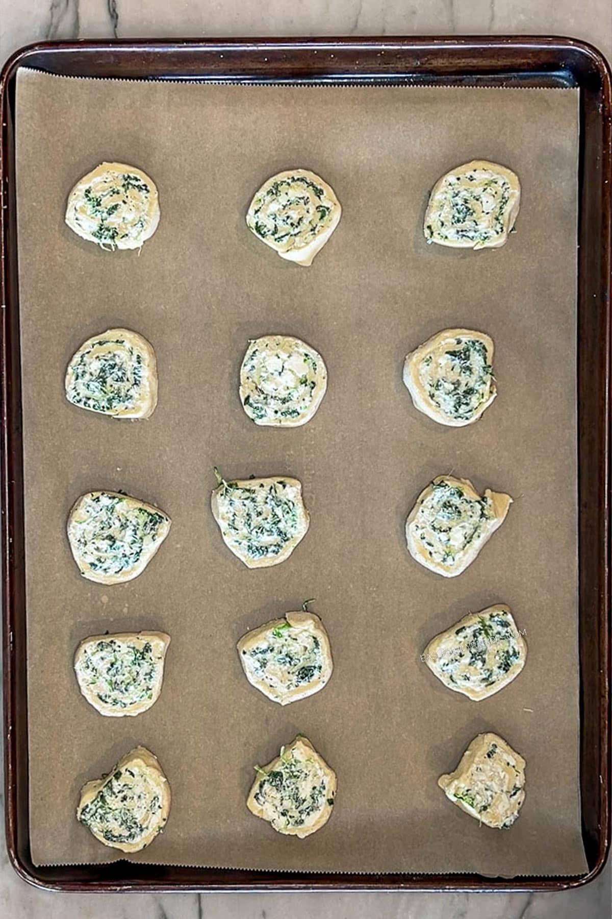 Spinach feta puff pastry swirls on parchment paper lined baking sheet. On a wooden background.