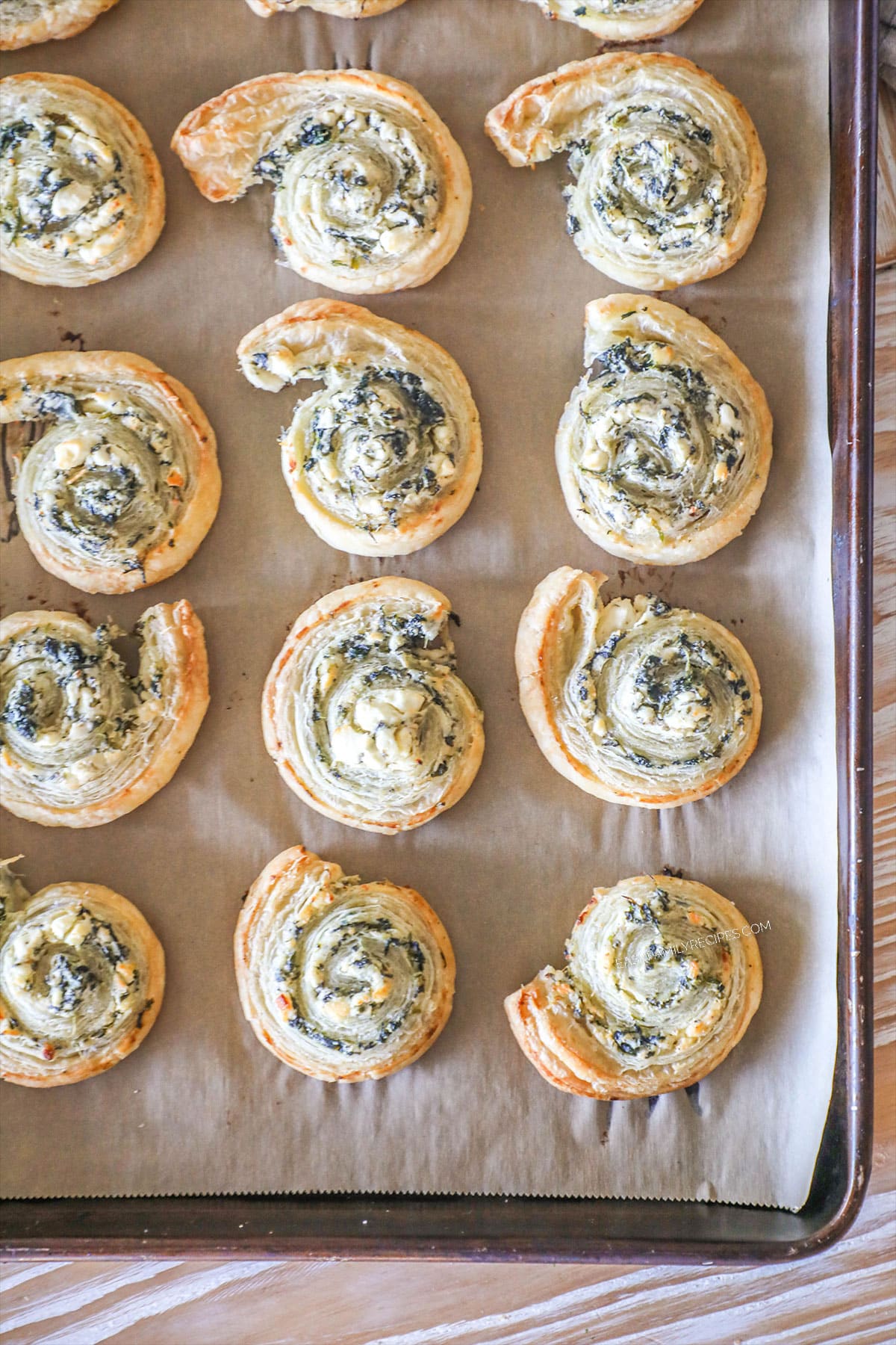 Spinach feta puff pastry swirls on parchment paper lined baking sheet. On a wooden background.