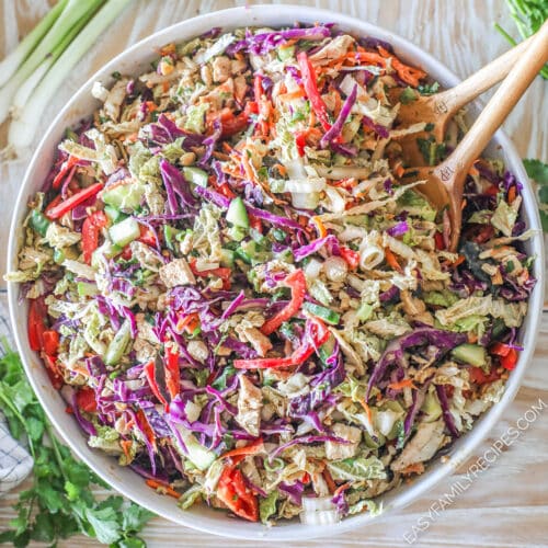 Thai Style Chicken Salad with Peanut Dressing in a large white bowl with wooden spoons. On a wooden backdrop
