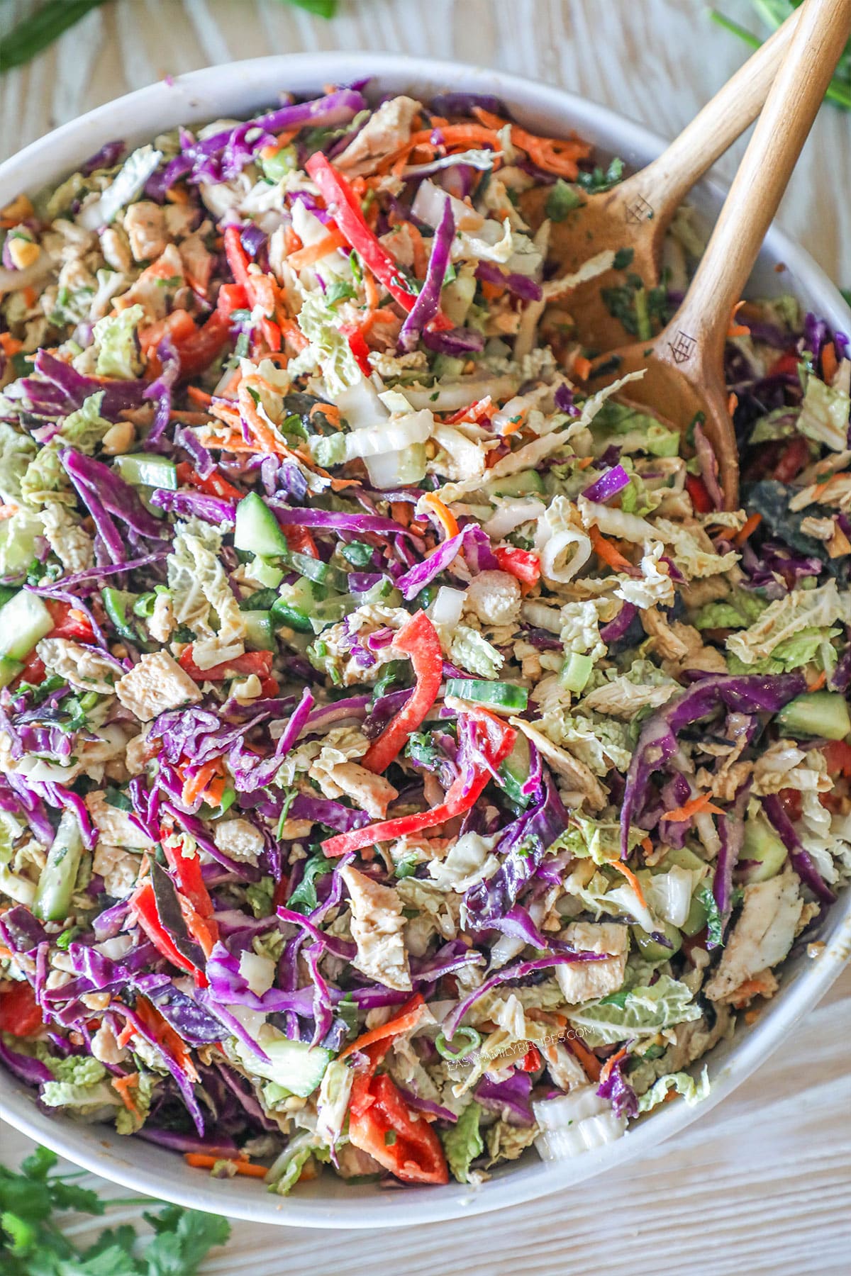 Thai Style Chicken Salad with Peanut Dressing in a large white bowl with wooden spoons
