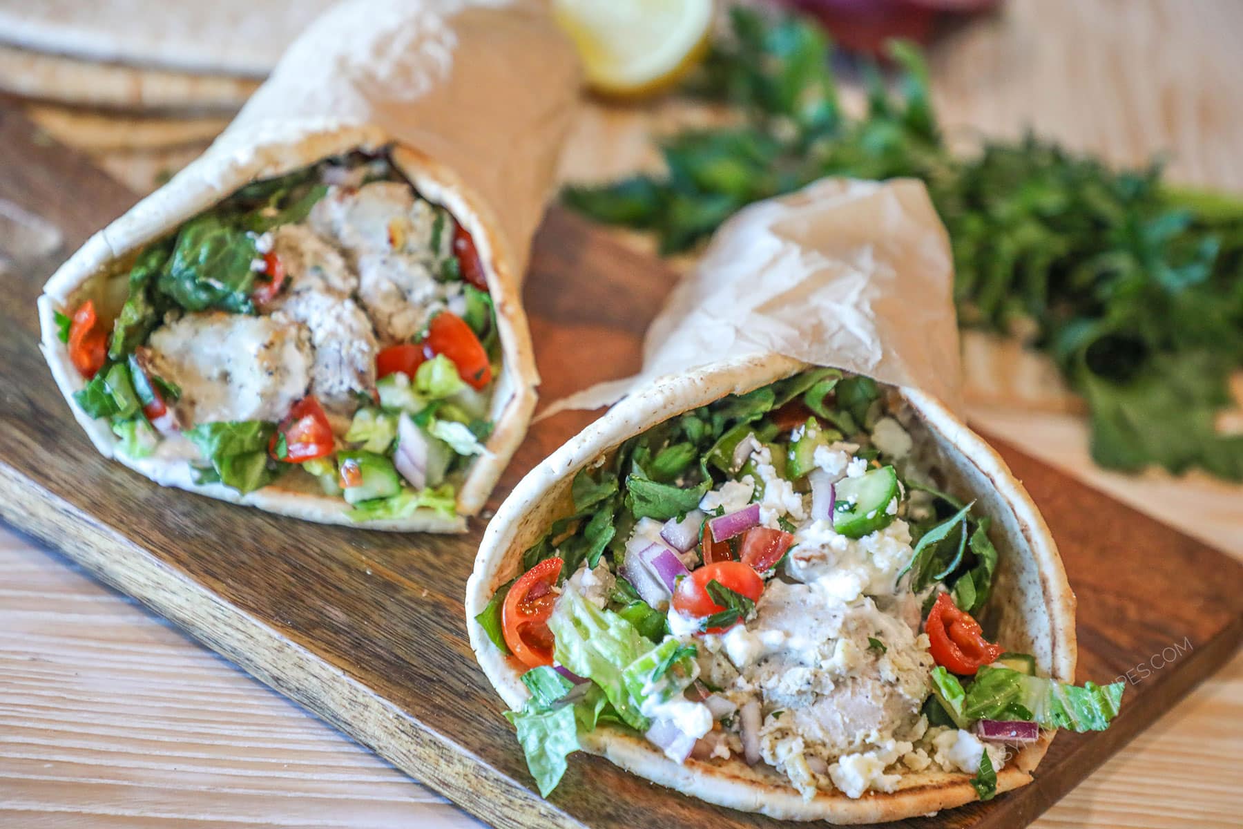 Two baked chicken gyros on a wooden board.