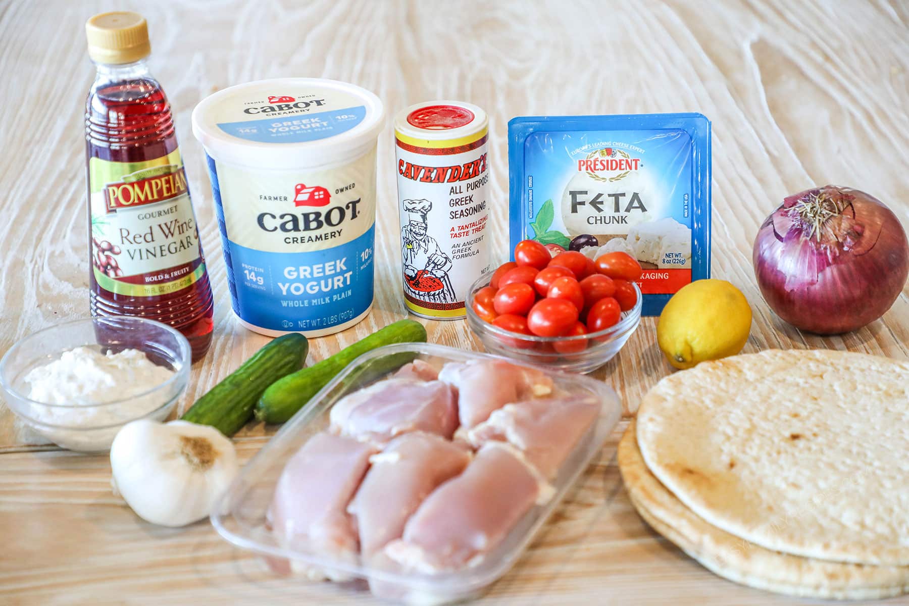 Ingredients needed to make baked chicken gyros on a wooden background.