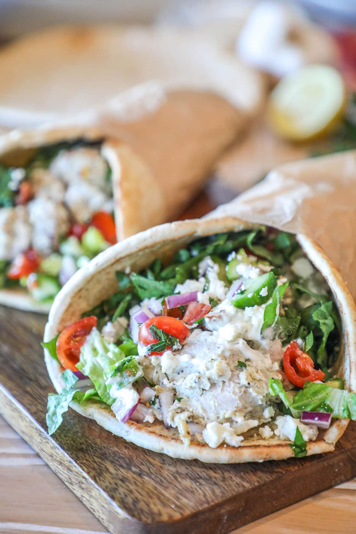Baked chicken gyro on a wooden board with lettuce, tomatoes and onions on top.