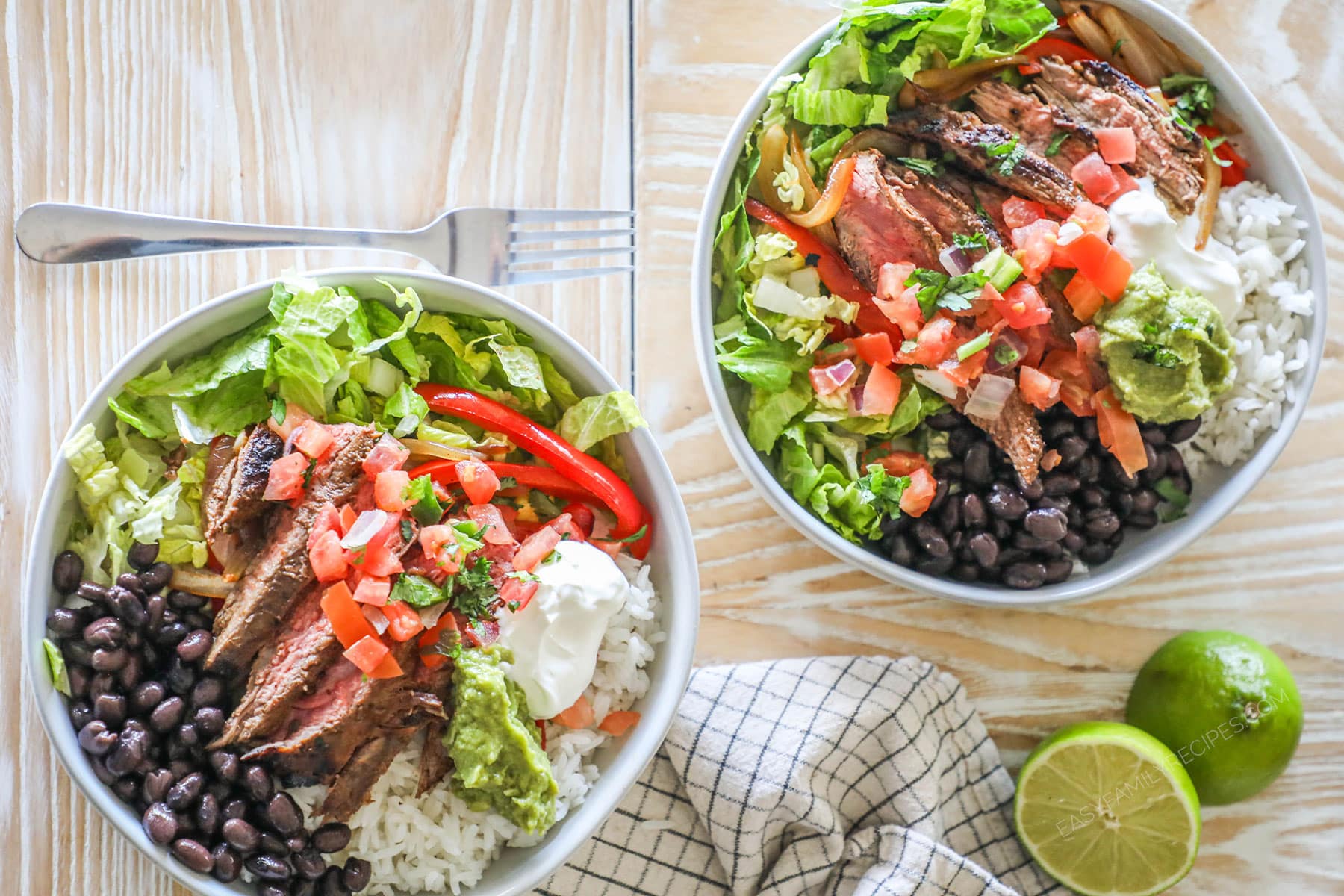 Two carne asada bowls both topped with toppings, on a wooden background.