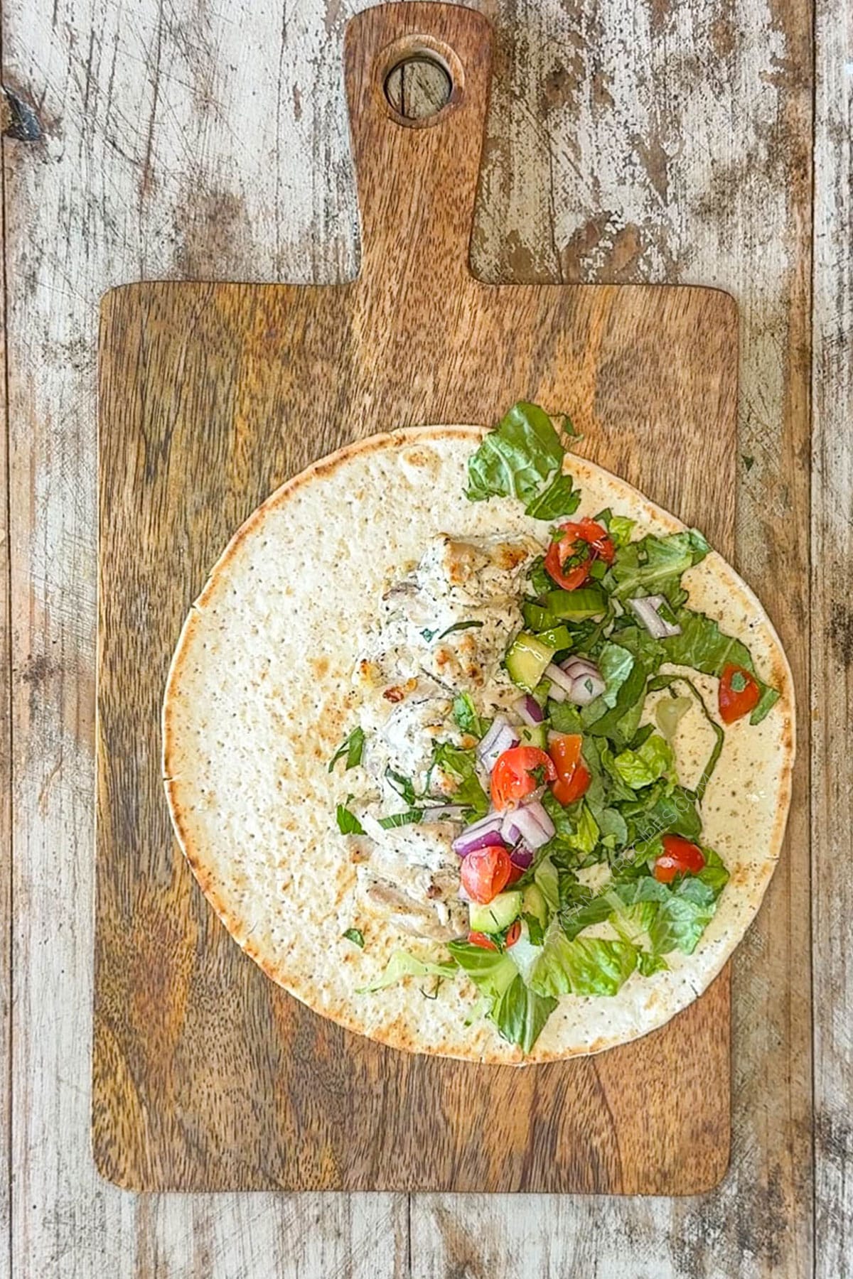 Adding lettuce, onions, and tomatoes to the chicken in a pita round.