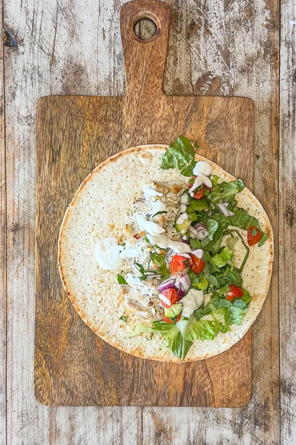 Drizzle of tzatziki sauce added to the baked chicken gyros in a pita round.