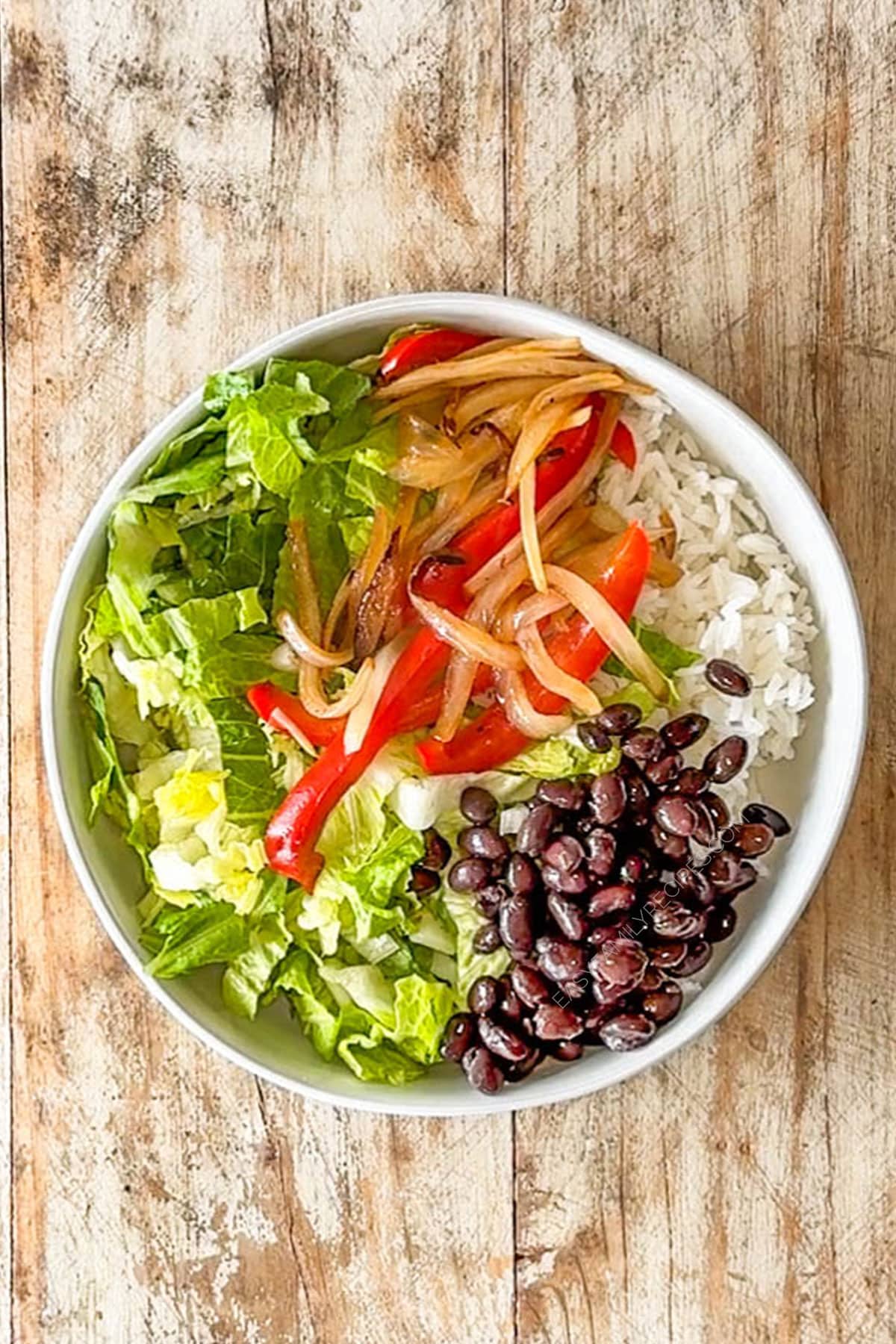 Assembling the carne asada bowls with rice, lettuce, fajita veggies and beans.