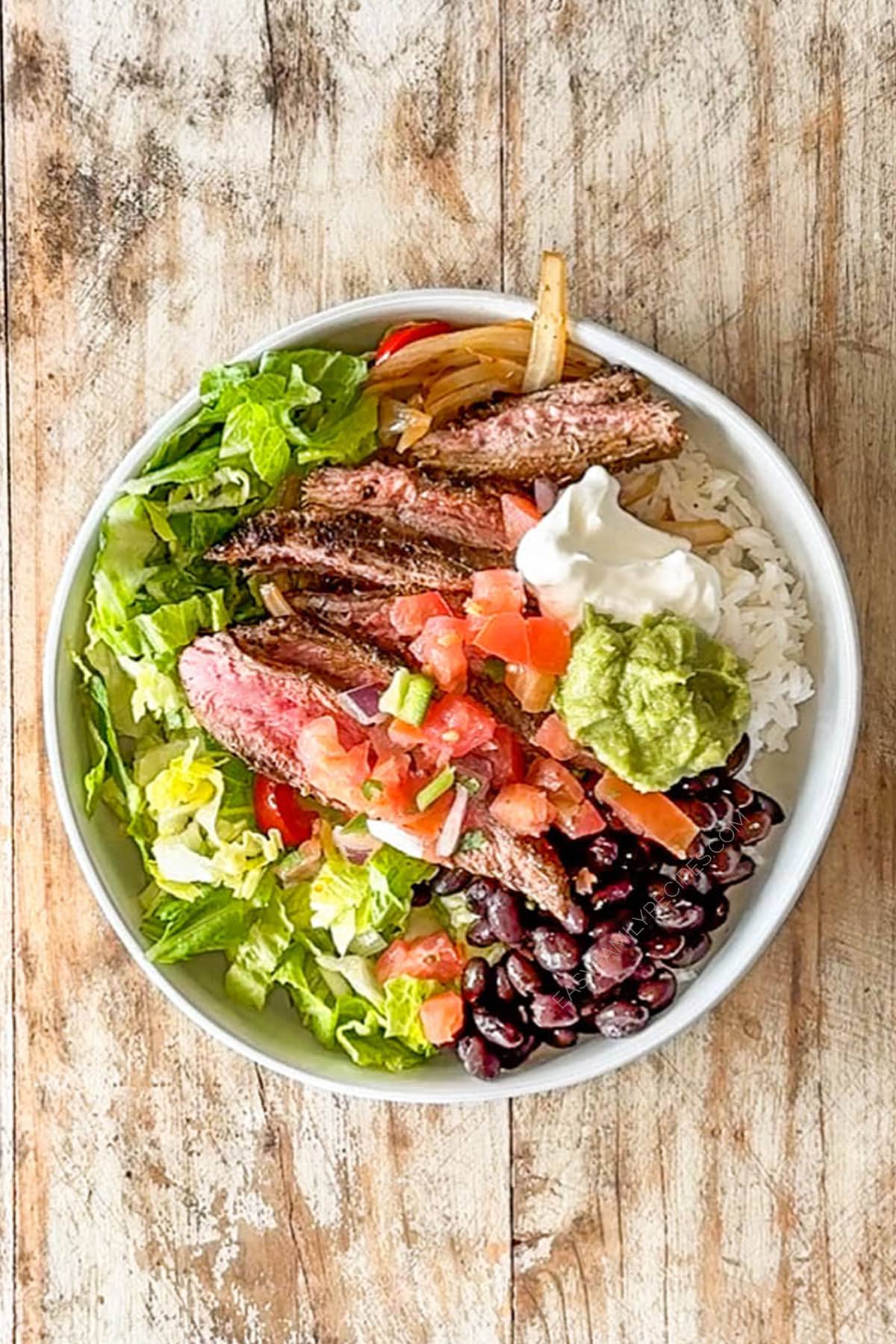 Overhead shot of a carne asada bowl on a wooden background.