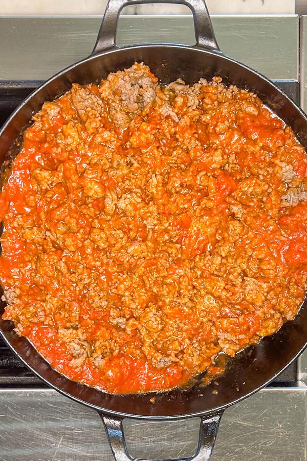 Marinara sauce added to the browned ground meat in a skillet.