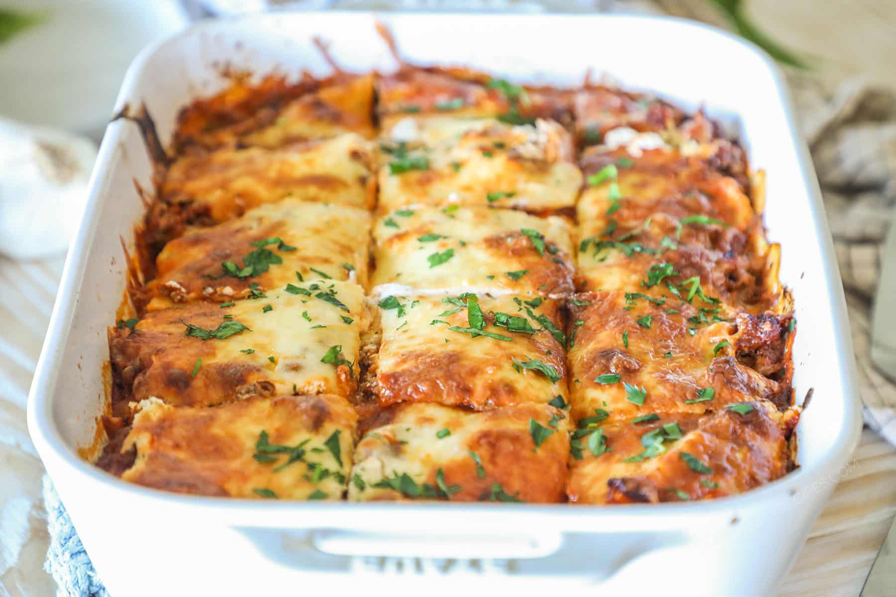 Side view of baked million dollar ravioli in a white baking dish, sliced into squares.