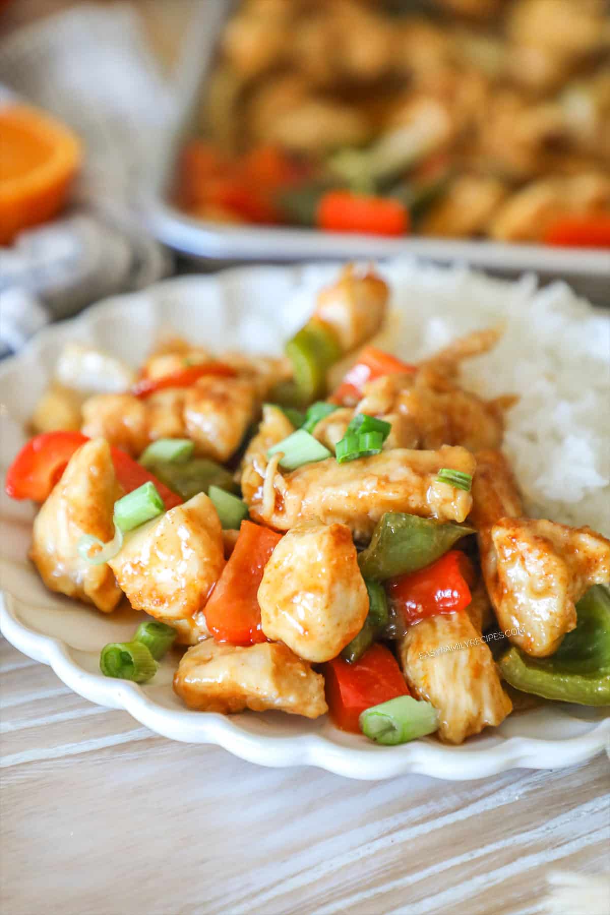 Individual serving of sheet pan orange chicken with white rice. On a white plate. Sheet pan in background.