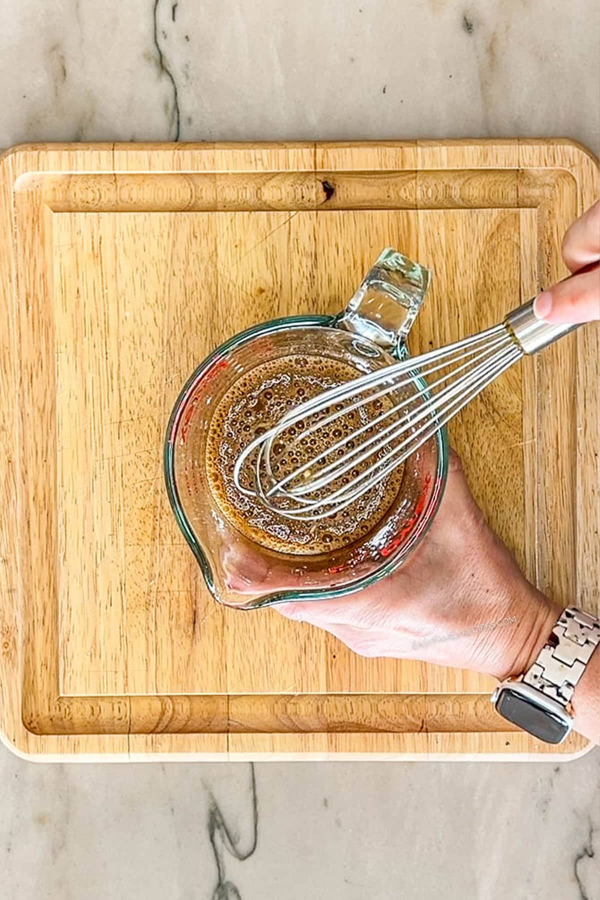 Step two of making sheet pan orange chicken. Bowl of ingredients for sauce whisked together. On a wooden board
