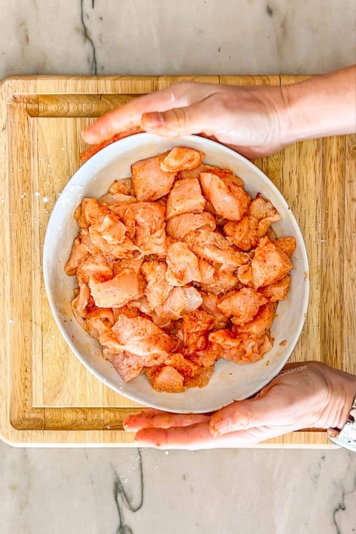 Step four of making sheet pan orange chicken. White bowl of chicken bites with seasoning mixed throughout.