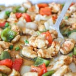 Pan of sheet pan orange chicken with spoon lifting off the pan